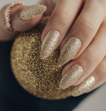 Golden nail manicure. Holiday style bright manicure with glitter. Beautiful hands. Close up photo.