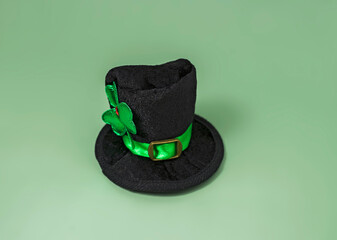 black leprechaun hat with green ribbon and clover shamrock on green background, abstract background for st. patrick's day