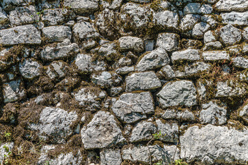 An old stone wall covered with moss and withered grass. The texture of the stone back