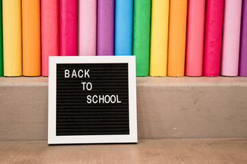 Oversized rainbow colored pencils with small letter board sign that reads "Back to School"