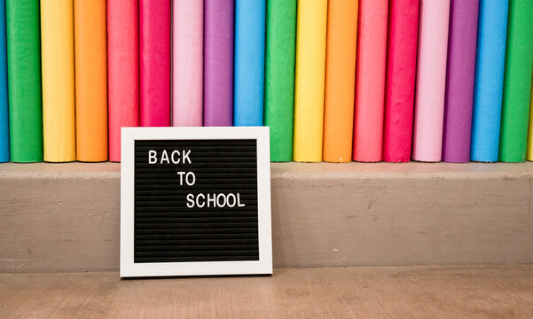Oversized rainbow colored pencils with small letter board sign that reads "Back to School" - Powered by Adobe