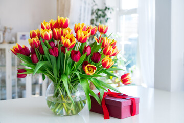 Huge spring bouquet of tulips in vase and gift box on the table with light classic interior design...