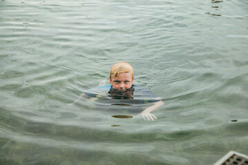 Blonde boy swimming with head just above water in clear saltwater pool on holiday in Newcastle,...