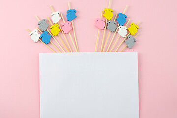 White envelope for congratulations on a pink background with wooden rabbits on sticks. Easter concept.