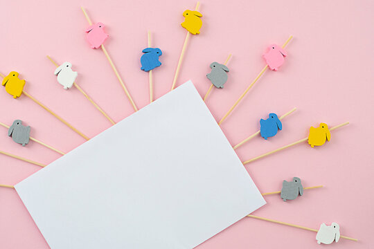White envelope for congratulations on a pink background with wooden rabbits on sticks. Easter concept.