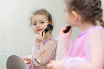 Happy little cute girl playing with her mother's cosmetic, selfcare, beauty procedure Treatment, makeup, visage, powdering face in front of mirror at home.