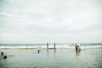 People swimming at the Bogey Hole in Newcastle, NSW on an overcast day with rough surf
