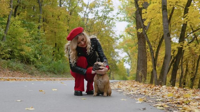 Young beautiful woman walking in autumn park with funny french bulldog