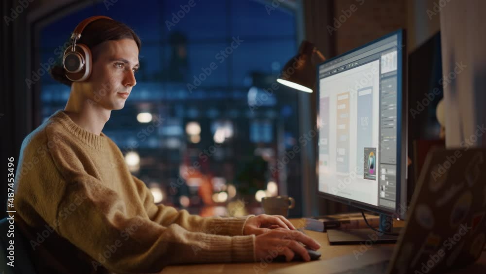 Poster Young Handsome Man Working from Home on Desktop Computer in Stylish Loft Apartment in the Evening. Creative Designer Developing Innovative Mobile Interface. Urban City View from Big Window.