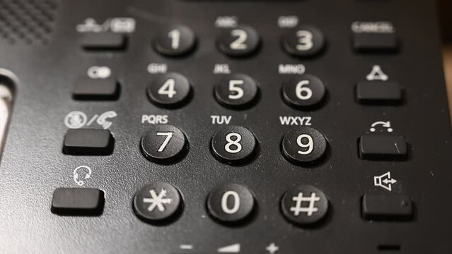 Dialing telephone keypad in office. Black phone, close up.