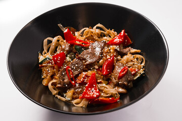 Fried noodles with meat, chili peppers, black and white sesame seeds in a black plate