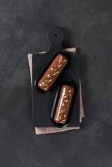 Chocolate nut cake in the form of a bar, with mirror glaze on a serving plate on a dark gray background. Top view