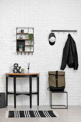 Stylish interior of room with light brick wall, backpack and table with decor