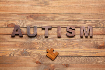 Word AUTISM and puzzle piece on wooden background