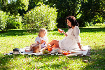 young pretty pregnant brunette woman having fun with her daughter on picnic on green grass in park,...