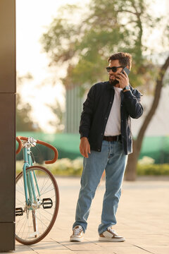 Stylish Bearded Man With Bicycle Talking By Mobile Phone In City