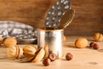 Tin can with boiled condensed milk and tasty walnut shaped cookies on wooden background