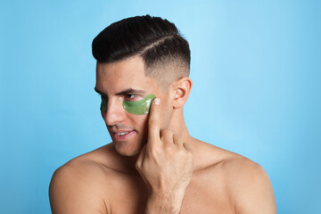 Man applying green under eye patch on light blue background
