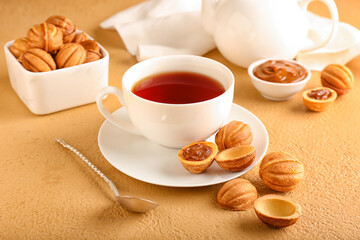 Tasty walnut shaped cookies with boiled condensed milk and cup of tea on beige background