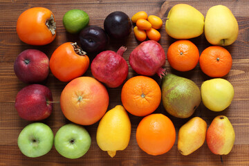 Different types of fruits on a brown wooden table. View from above. Closeup. Persimmons, apples, plums, pomegranates, pears, oranges, tangerines, bergamot, kumquat, lime, grapefruit