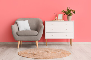 Comfortable armchair, chest of drawers and wicker carpet in room interior