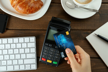 Woman with credit card using modern payment terminal at wooden table, top view