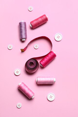 Sewing threads with measuring tape and buttons on pink background