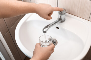 Man with glass turning off tap in bathroom, closeup