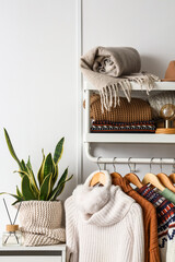 Rack with stylish sweaters and ear muffs near light wall