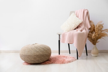 Chair with pillow, plaid, vase and pouf near light wall