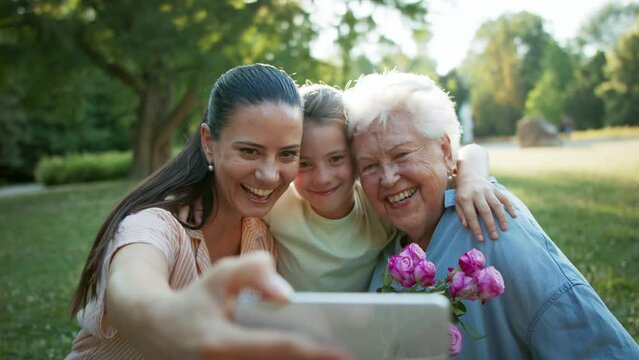 Small girl with mother and grandmother in a park, taking selfie when celebrating birthday.
