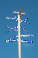A steel metal pole with multiple directional arrows listing city names and distances such as...
