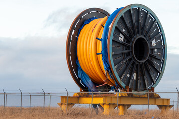 Bulk sub-sea industrial glass fiber optic cable on a metal spool on a ship's stand. The orange data...