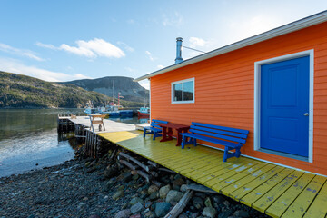 The exterior wall of an orange color wooden boathouse with a vibrant blue door, closed glass...