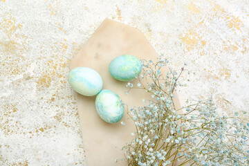 Board with beautiful Easter eggs and gypsophila flowers on light background