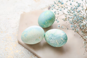 Board with beautiful Easter eggs and gypsophila flowers on light background, closeup