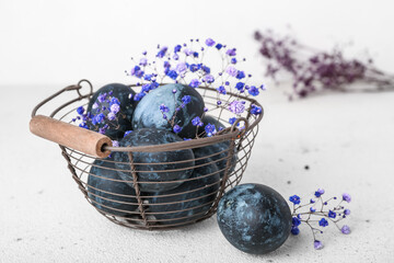 Basket with beautiful Easter eggs and gypsophila flowers on light background