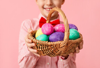 Funny little boy holding basket with Easter eggs on pink background, closeup