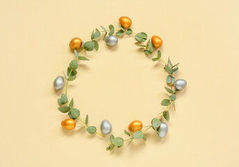 Frame made of Easter eggs and eucalyptus branches on beige background