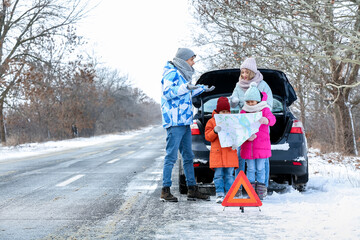 Parents and their little children with map near broken car on snowy winter day