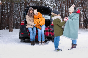 Happy children with their parents and car in forest on snowy winter day