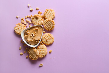 Tasty peanut cookies and bowl with butter on lilac background
