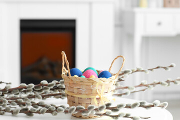 Basket with painted Easter eggs and pussy willow branches on table at home