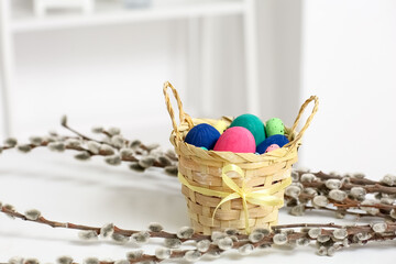 Basket with painted Easter eggs and pussy willow branches on table at home