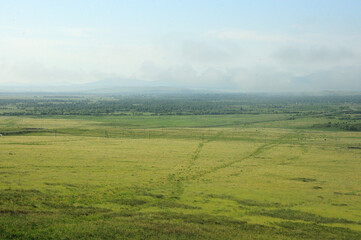 Endless steppe and a large forest at the foot of a mountain range with peaks in the clouds. © Алексей Желтухин