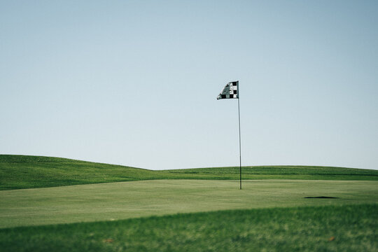 Golf flagstick waving in a green field with a light blue sky in the background