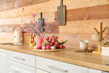 Easter eggs and bouquet of tulips on counter near wooden wall in kitchen interior