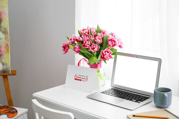 Workplace with modern laptop, tulips, cup of coffee and greeting card with text HAPPY WOMAN'S DAY