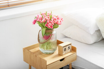 Bouquet of tulips and wooden cube calendar with date MARCH 8 on bedside table. International Women's Day celebration