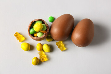 Chocolate Easter eggs with different candies on light background